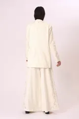 Blazer color crema con solapas de muesca, cierre frontal con dos botones, bolsillos delanteros con solapa y mangas largas con bordados calados.