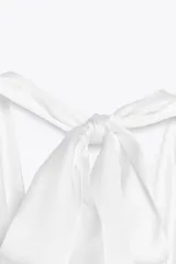Top blanco de tejido satinado con cuello halter drapeado ajustable con lazada en el cuello y espalda descubierta con lazada.