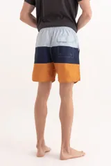 Short de baño con diseño de bloques de color horizontal en tonos celeste, azul marino y mostaza, con cintura elástica y cordón ajustable.