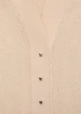Jersey de punto fino color beige, con cuello camisero, manga corta y cierre frontal con botones pequeños. Diseño entallado de canalé.