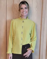 Camisa color verde lima con cuello alto tipo gorguera, cierre frontal con doble botonadura y mangas largas con puños con volados. Presenta costuras decorativas visibles en contraste.