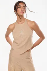 Top halter color beige de tencel, con diseño cruzado en el cuello y detalle de bordado a mano plateado en el frente con forma de sol o estrella radiante.