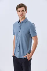 Camisa de piqué lisa color celeste, de manga corta, con cuello camisero y cierre frontal de botones oscuros.