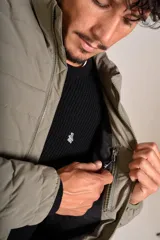 Campera puffer de corte clásico en color beige, con cierre frontal, cuello alto y puños elásticos. Presenta un diseño acolchado horizontal y un pequeño logo bordado en el pecho.