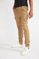 Pantalón cargo color beige de corte slim, con cintura elástica y cordón ajustable. Presenta bolsillos laterales con solapa y velcro, y puños elásticos en los tobillos.