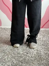 Pantalón de tela deportiva con felpa en color negro, de corte holgado y diseño con presillas en los tobillos para ajustar con lazo.