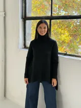 Sweater de punto color negro con cuello alto tipo polera, diseño holgado y corte asimétrico con la parte trasera más larga.