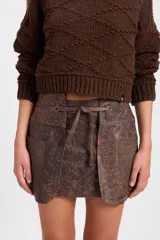 Minifalda de cuero con efecto desgastado, de silueta recta y diseño de capas frontales superpuestas. Incluye un lazo ajustable en la cintura que pasa por ojalillos metálicos y bolsillos laterales integrados.