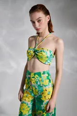 Top strapless con estampado floral en tonos verde y amarillo, con tirantes finos al cuello y detalle de nudo en el centro del busto.