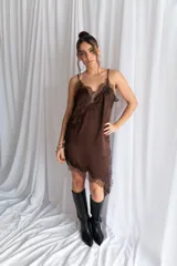 Vestido corto de satén negro, con tirantes finos, escote en V y detalles de encaje en el escote, el lateral y el dobladillo asimétrico.