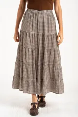 Falda larga de corte evasé con diseño de cuadros vichy en tonos marrón y blanco. Presenta una cintura elástica y un diseño de tres volados horizontales que aportan volumen y movimiento.