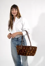 Cartera tipo tote de tamaño mediano, confeccionada en cuero con pelo con un diseño estampado de manchas en tonos marrones. Posee doble asa de hombro en cuero liso marrón y cierre superior.