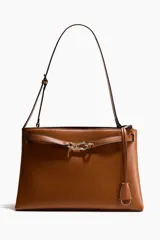 Cartera de hombro color tostado, fabricada en tejido revestido, con correa ajustable y un divisor interior que crea dos compartimentos, además de un compartimento interior con cierre. Presenta una trabilla decorativa con mosquetón metálico dorado en la parte delantera y una etiqueta extraíble.