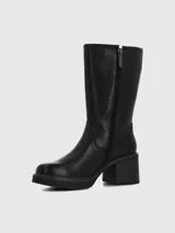 Bota de caña media confeccionada en cuero negro, con taco cuadrado y suela con plataforma. Presenta un diseño minimalista con costuras reforzadas y detalle de logo metálico en la parte superior de la caña.