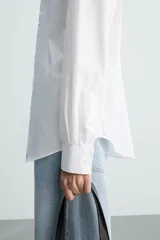 Camisa blanca de corte slim fit, confeccionada en tejido de algodón. Presenta cuello italiano, manga larga con puño abotonado y cierre frontal de botonadura.