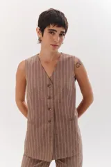 Chaleco largo color blanco con rayas verticales finas color beige, con cuello en V y cierre frontal con botones marrones. Incluye pañuelo al cuello con estampado de lunares y rayas.