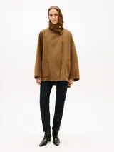 Abrigo de corte oversize confeccionado en mezcla de lana de doble cara, color marrón. Presenta cuello chimenea, cierre frontal con un botón visible y otro oculto, y dos bolsillos delanteros de parche.