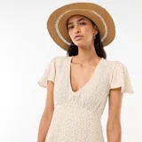 Vestido corto de corte evasé, con estampado floral sutil en tonos rosados y verdes sobre base blanca. Presenta escote en V y mangas cortas tipo mariposa.