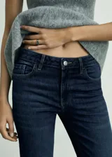 Jeans tiro medio de corte flare confeccionados en denim azul oscuro, con diseño de cinco bolsillos, trabillas para cinturón y bajo deshilachado.