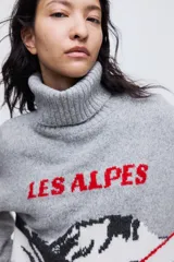 Sweater de punto gris con cuello alto acanalado, diseño jacquard frontal con paisaje de montaña y teleférico en colores blanco, negro y rojo, y hombros caídos.