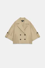 Trench corto de color beige, con cuello de solapa, cierre cruzado con botones y mangas cortas con vuelta y trabilla con botón.
