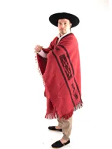 Poncho de tejido de punto con diseño geométrico en colores negro, rojo y beige, con terminaciones de flecos en el ruedo y escote en V.