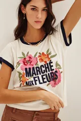 Remera de algodón color crema con cuello y bordes de mangas en contraste azul marino. Presenta un diseño frontal con bordados de flores coloridas y la inscripción 'MARCHÉ aux FLEURS' en letras azules.