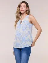 Blusa de lino y rayón color beige con estampado floral en tonos celestes, sin mangas, con escote redondo y detalle de tres aros metálicos plateados entrelazados en el frente.