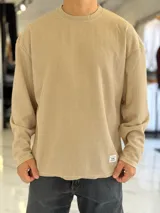 Buzo oversize de tejido waffle en color beige, con cuello redondo y manga larga, con pequeña etiqueta de marca en el dobladillo inferior.