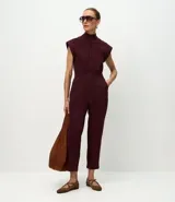 Mono largo de sarga color bordó, con cuello alto, cierre frontal oculto, sin mangas y ajuste en la cintura con botón y trabillas. Presenta bolsillos laterales y corte recto.