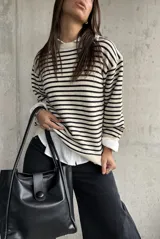 Sweater de punto a rayas horizontales en color natural y negro, con cuello redondo y mangas largas con detalle de botones en los puños.