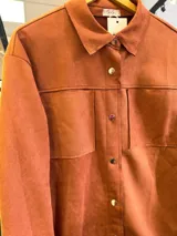 Sobrecamisa de gamuza color terracota, con cierre frontal de botones metálicos, cuello camisero y bolsillos frontales tipo parche.