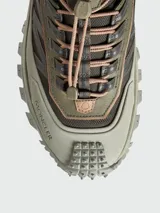 Championes de trail running Moncler modelo Trailgrip GTX, en tonos verde oliva y beige. Presentan un diseño robusto con suela dentada Vibram, sistema de cordones de ajuste rápido y refuerzo en la puntera con el logo de la marca.