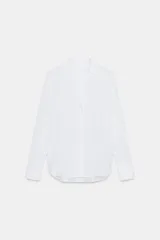 Camisa blanca de cuello solapa, escote pico y manga larga. Presenta un bajo asimétrico y cierre frontal con botones.