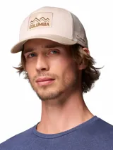Gorro tipo trucker Columbia Mesh Snap Back de color beige, con visera curva en tono tostado, paneles traseros de malla transpirable y un parche frontal bordado con diseño de montañas y el logotipo de la marca.