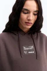 Canguro de algodón con capucha y bolsillo frontal, de diseño urbano y corte holgado. Presenta un parche rectangular en el pecho con detalles gráficos y el logo de la marca Mistral.