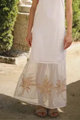 Vestido largo de lino puro color blanco, con escote cuadrado y finos tirantes ajustables. Cuenta con el bajo transparente y delicadamente bordado con palmeras doradas.