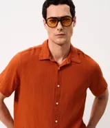 Camisa de manga corta color mostaza, confeccionada en algodón con textura, cuello inglés y cierre frontal de botones.