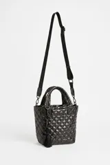 Cartera tote negra de diseño matelasse acolchado, con doble asa de mano y correa larga ajustable con inscripciones. Cuenta con cierre superior y detalle de llavero con borla colgante.