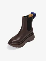 Bota tipo Chelsea de cuero de oveja color marrón, con paneles elásticos laterales negros y suela chunky dentada. Incluye un tirador trasero con detalle tejido en azul.