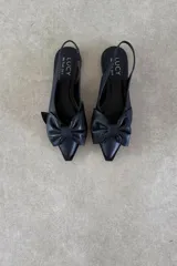 Zapato chatita destalonada de cuero negro, con punta fina y detalle de moño grande en el empeine.