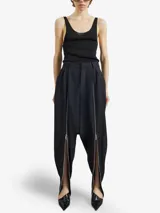Pantalón negro de lana virgen, inspiración sarouel, con pliegues delanteros estructurados y cierres metálicos frontales de largo completo.