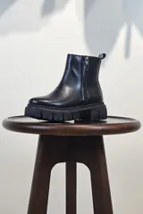 Bota de caña corta color marrón, con cierre lateral y suela track negra de goma con plataforma.