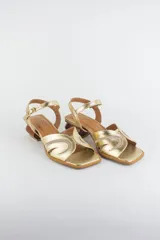 Sandalias doradas con capellada de cuero metalizado y malla, puntera cuadrada, tira ajustable al tobillo y taco geométrico de madera.