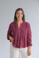 Blusa de manga larga color bordó con cuello mao y cierre frontal de botones. Presenta detalles de bordados florales y calados en el frente, con un corte holgado y puños elásticos.