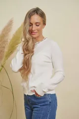 Saco blanco de punto con cuello redondo y detalles de strass en el escote. Tiene mangas largas y cierre frontal con botones.