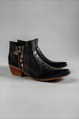 Bota corta de cuero negro con diseño combinado, punta fina y taco geométrico de madera. Presenta detalles en textura croco, apliques laterales con cierre, detalles metalizados y talón con acabado texturizado.