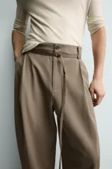 Pantalón de corte balloon fit en color gris, confeccionado en tejido con viscosa. Presenta pliegues frontales, cintura con cinturón integrado a contraste, bolsillos laterales y bolsillos traseros de vivo.