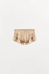 Shorts satinados color beige, con tiro medio, cintura elástica y diseño fluido. Presentan bordados florales en los laterales y volantes con puntillas en el bajo.