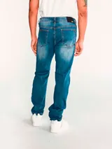 Jeans de mezclilla azul con calce slim, diseño clásico de cinco bolsillos, cierre de cremallera y botón metálico. Presenta efecto desgastado en los muslos y costuras en tono contrastante.